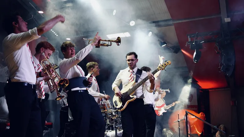Die Band in weißen Hemden mit erhobenen Instrumenten im Scheinwerferlicht